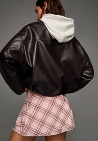 Bruine leren oversized jas met een grijze hoodie eronder, gecombineerd met een roze geruite minirok met dunne bruine lijnen.
