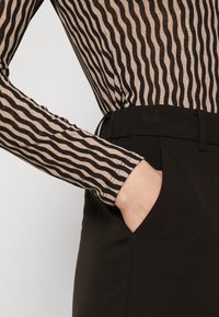 Langärmeliges Oberteil mit horizontalen schwarz-beigen Streifen, kombiniert mit schwarzen hoch taillierten Hosen, die ein seitliches Taschen-Design aufweisen.