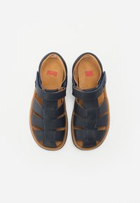 Jūras zila ādas sandaļi ar atvērtu pirkstu un papēdi, ar austas siksnas dizainu un regulējamu sprādzi. Tan krāsas iekšpuse un izteikta zīmola simbolika.