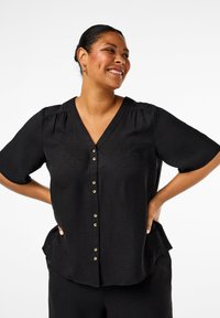 Black v-neck blouse with short sleeves, featuring gold buttons down the front and a textured fabric. Slightly curved hem and relaxed fit.