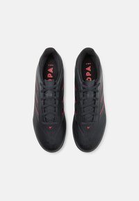Black athletic shoes with a smooth texture, featuring red accents and laces, a sleek profile, and a minimalist design.