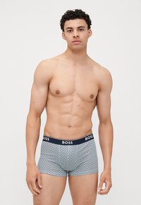 Boxer-briefs pour hommes en tissu bleu clair avec un motif géométrique rouge et bleu marine. Doté d'une ceinture bleu marine avec le logo "BOSS". Texture lisse.