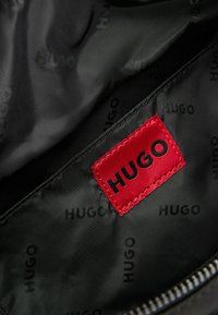 Interno in tessuto nero con motivo ripetuto "HUGO"; dotato di un'etichetta rossa con "HUGO" in lettering nero; texture liscia, chiusura con zip.