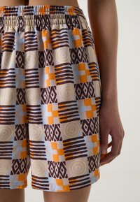 Pantalones cortos multicolor con una mezcla de patrones geométricos en naranja, azul y marrón. Hechos de tela ligera con una cintura elástica.