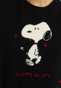 Zwarte trui met een gebreid Snoopy-ontwerp in het wit, met accenten van rode harten en tekst die "Snoopy Est. 1950" zegt.