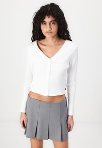 White ribbed long-sleeve cropped cardigan with a V-neck and front buttons, paired with a gray pleated mini skirt.