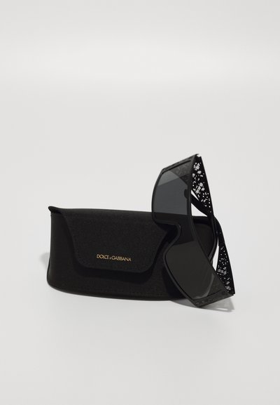 Occhiali da sole neri con dettagli intricati a pizzo sulla montatura, accompagnati da una custodia morbida nera con accenti dorati.