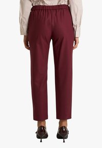 Pantaloni a sigaretta color bordeaux con vita elasticizzata, consistenza liscia e linee pulite. Abbinati a décolleté lucide con punta affilata.