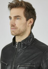 Schwarze Lederjacke mit hohem Kragen, ausgestattet mit Reißverschlusstaschen und gesteppten Details auf den Schultern. Glatte Textur, modernes Design.
