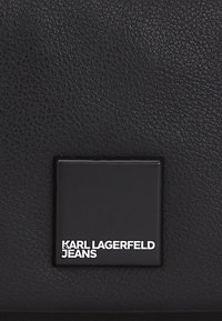 Borsa a tracolla in pelle nera con superficie texturizzata e un plate logo rettangolare impresso con "KARL LAGERFELD JEANS" in bianco.