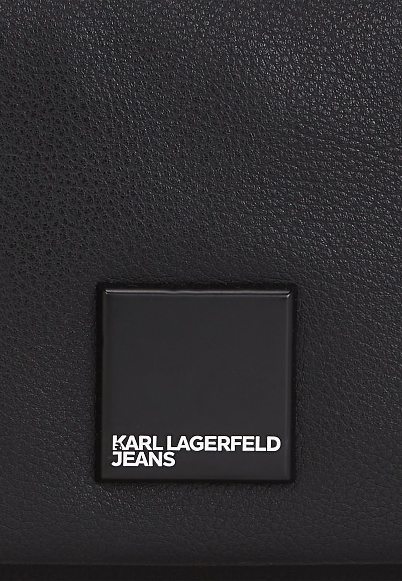 Czarna skórzana torebka z teksturowaną powierzchnią i prostokątną tabliczką z logo wytłoczonym "KARL LAGERFELD JEANS" na białym tle.