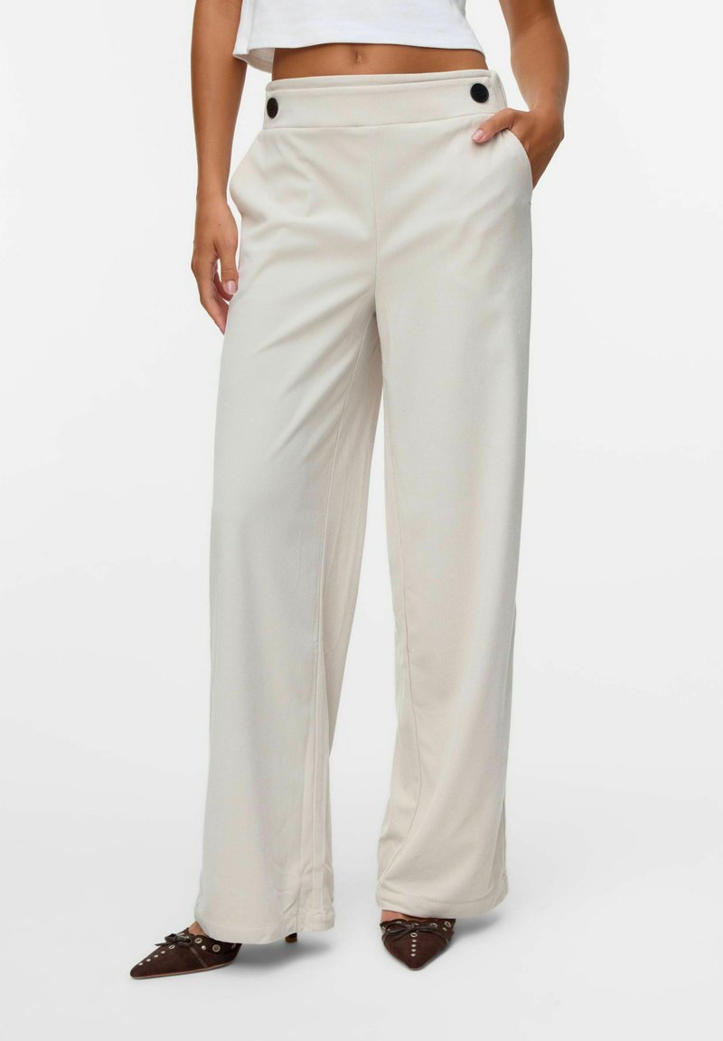 Pantaloni ampi color beige chiaro realizzati in un tessuto morbido, con una texture liscia, tasche frontali e due bottoni neri decorativi in vita.