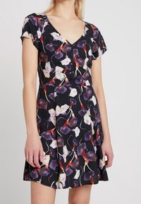 Abito floreale con scollo a V, maniche corte e un corsetto aderente che si allarga in una gonna. Il tessuto ha una base nera con motivi floreali colorati.