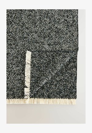 Vävd svart och vit matta med fiskbensmönster och fransiga kanter, som visar en strukturerad textil och en geometrisk design.