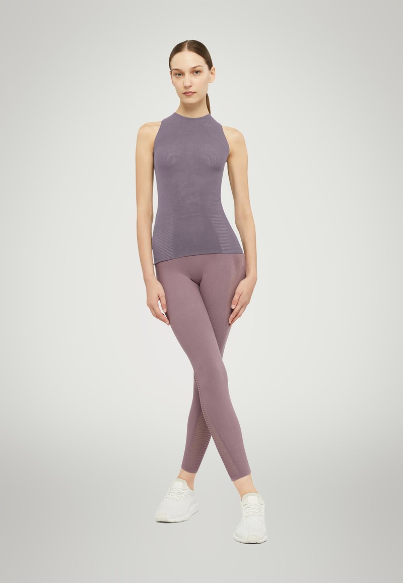Top aderente senza maniche di un leggero colore viola con un design testurizzato, abbinato a leggings a vita alta coordinati che presentano motivi laterali e una leggera lucentezza.