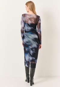 Robe longue à manches transparentes avec une silhouette ajustée, présentant un motif abstrait bleu et noir, un tissu transparent et un ourlet mi-long.