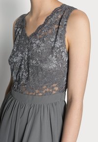 Robe grise avec un corsage en dentelle orné de motifs floraux, un décolleté festonné et une jupe fluide à taille froncée.