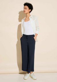 Marinblå vida byxor med elastisk midja, tillsammans med en vit linne och en ljus knapp-up skjorta. Bärs med vita sneakers.