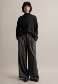 Μαύρο πλεκτό πουλόβερ με ζιβάγκο και ραμμένα μανίκια, σε συνδυασμό με γκρι παντελόνια με ψηλή μέση και φαρδύ πόδι καθώς και μαύρα αθλητικά παπούτσια με ψηλή σόλα.