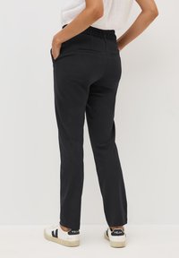 Sorte, tætsiddende sweatpants med elastisk talje, sidelommer og en glat overflade, parret med hvide sneakers med sorte detaljer.