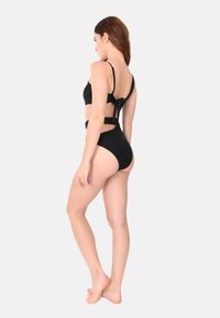 Costume intero nero con spalline regolabili, dettagli laterali con tagli e schiena legata. Tessuto liscio con finitura opaca.