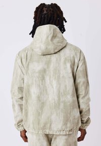Giacca a cappuccio verde chiaro con un motivo testurizzato simile a una acquerello. Presenta polsini elasticizzati e una vestibilità comoda, realizzata in tessuto leggero.