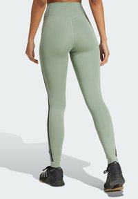 Leggings a vita alta e aderenti in morbido tessuto verde chiaro con strisce nere sui lati e cuciture piatte. Presentano un girocoda curvo e una finitura minimale.