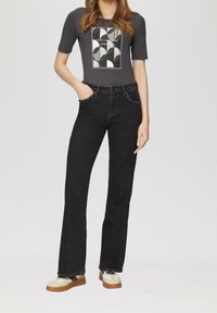 Jeans neri a vita alta con gambe dritte, abbinati a una maglietta grigia a maniche corte con una stampa geometrica in bianco e nero.