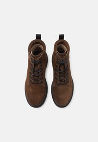 Paire de bottes en daim marron à lacets avec semelles noires et languettes de traction, vues de dessus sur un fond blanc.
