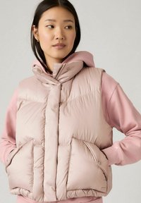 Lichtroze gewatteerde vest met hoge kraag en drukknoopsluiting, met twee voorkruiszakken en een zachte textuur. Draag het over een bijpassende roze hoodie.