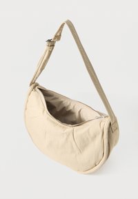 Μπεζ καπιτονέ τσάντα ώμου με καμπυλωτό σχήμα, κλείσιμο με φερμουάρ και ρυθμιζόμενο λουρί. Ομαλή υφή με απαλό, επενδυμένο φινίρισμα.