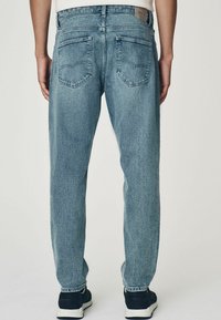 Jeanși de denim albastru deschis cu croială dreaptă, având două buzunare la spate și o ușoară decolorare. Purtați cu sneakers negri.