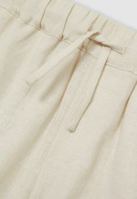 Beige linne tyg med en rynkad midja och en knytbar dragsko. Har subtila texturer och sömnadsdetaljer längs kanterna.