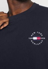 T-shirt navy a maniche corte in cotone, con un logo ricamato circolare che riporta il testo "NEW YORK" e "TOMMY HILFIGER".