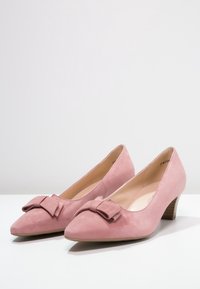 Pumps in suede rosa con punta affusolata e dettaglio a fiocco. Tacco in legno di altezza media. Texture liscia e design semplice ed elegante.