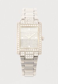 Srebrni pravokutni sat s kristalnim ukrasima, ukrašenim četvrtastim brojčanikom i metalnom narukvicom. Na brojčaniku je prikazan logo "GUESS".