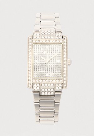 Reloj rectangular plateado con detalles de cristales, esfera cuadrada con piedras preciosas y pulsera metálica. Logotipo "GUESS" visible en la esfera.