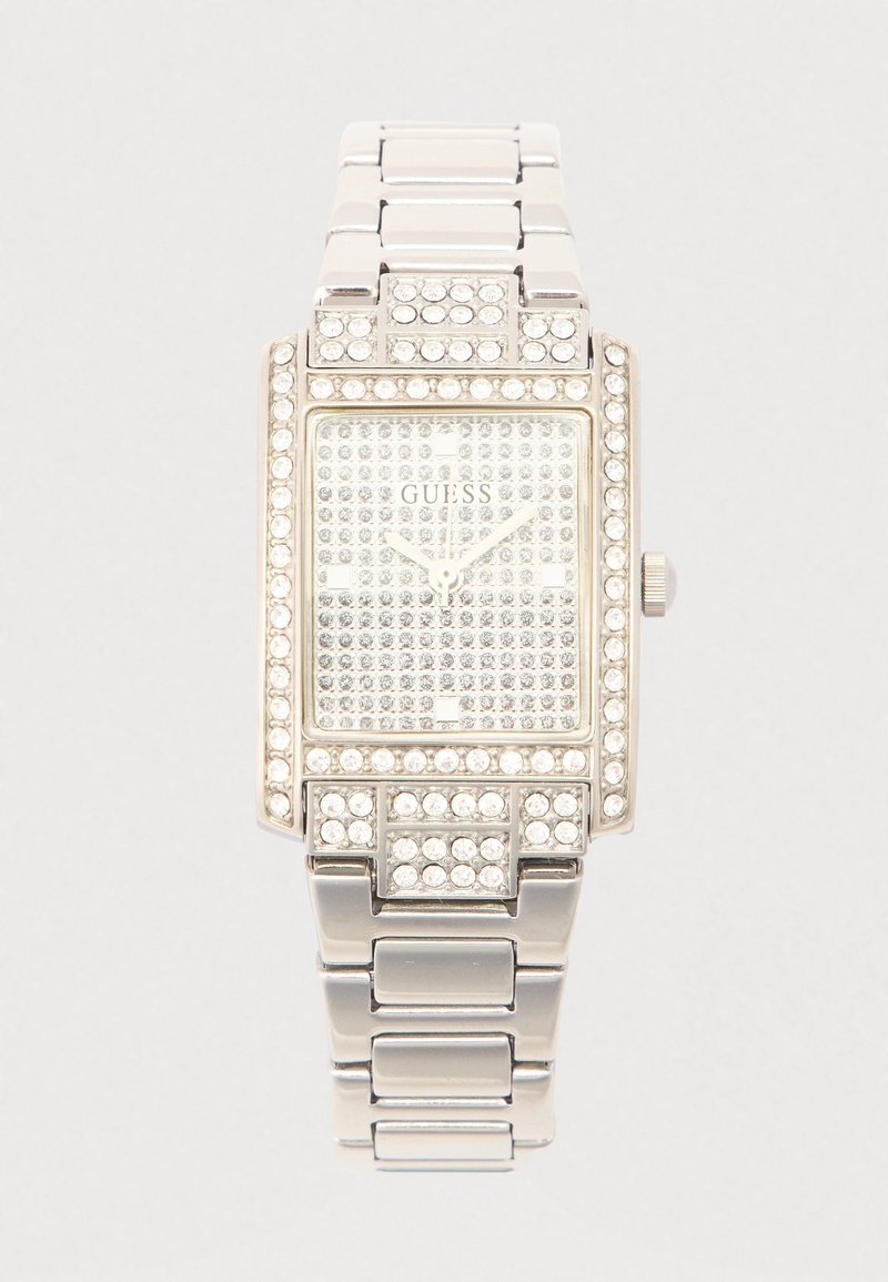 Srebrni pravokutni sat s kristalnim ukrasima, ukrašenim četvrtastim brojčanikom i metalnom narukvicom. Na brojčaniku je prikazan logo "GUESS".