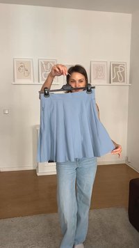 Gonna pieghe blu chiaro esposta su un gancio nero, caratterizzata da un tessuto liscio e un design a vita alta. Dettagli del tessuto testurizzati visibili.