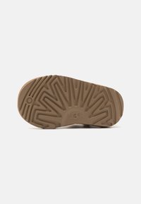 Light brown rubber sole with a textured, ridged pattern. Central logo embossed. Tapered shape with rounded edges.