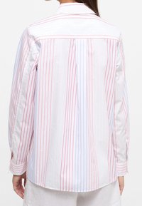 Vista trasera de una camisa blanca con rayas verticales rojas y azules, que cuenta con un collar estándar y mangas largas con puños.