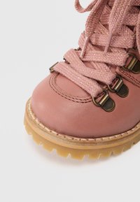 Bota de caminhada rosa em couro, com atacadores texturizados rosa, ilhós em metal e sola de borracha robusta. A ponta é arredondada com costura visível.