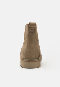 Stivaletto in suede marrone con punta rotonda e retro texture. Presenta una suola in gomma bassa e un accento di cucitura attorno al sottopiede.