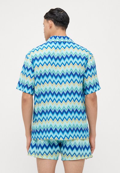 Súprava košele s krátkym rukávom a šortiek v cik-cak vzore s modrou, zelenou a krémovou farbou. Vyrobené z hladkej látky, s golierom.