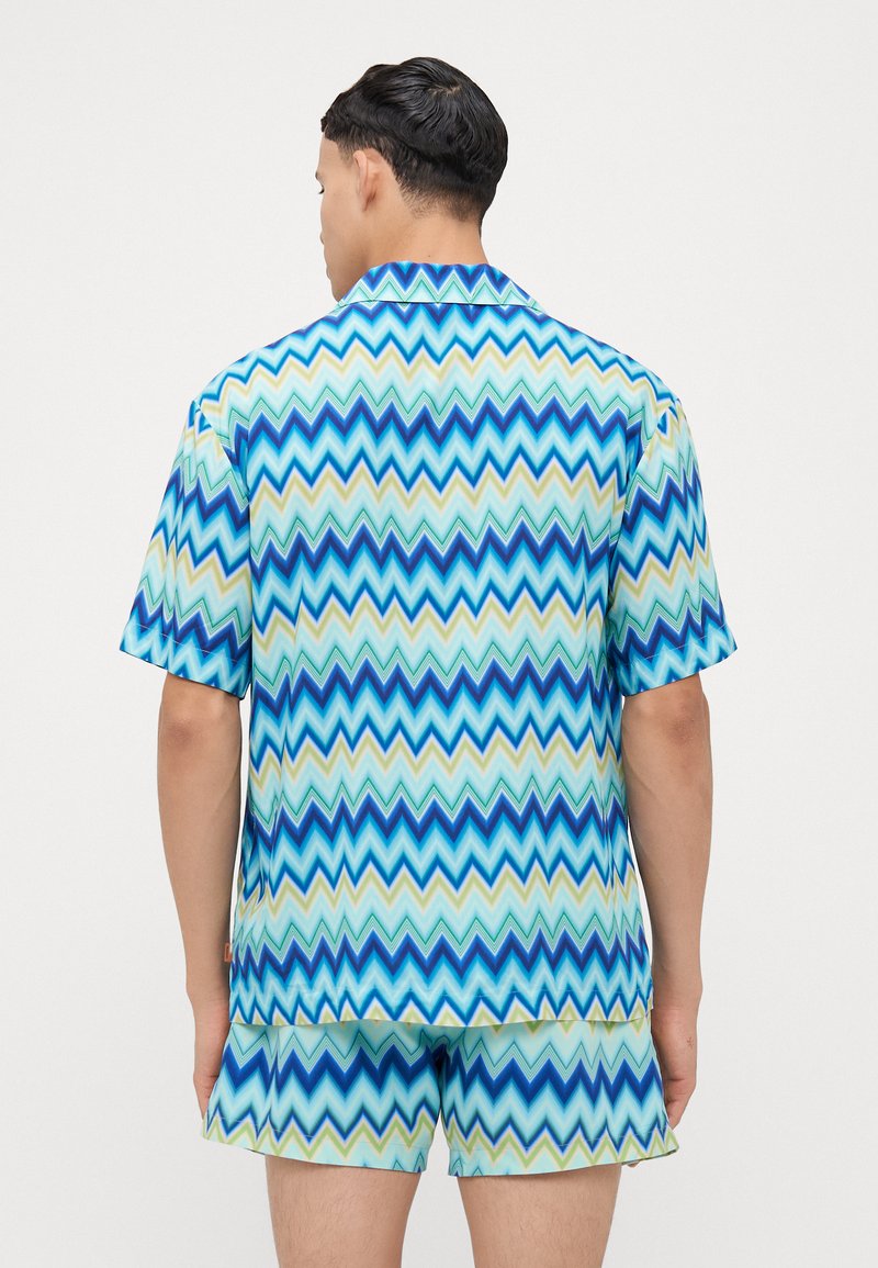 Set di camicia a maniche corte e pantaloni corti con motivo a zigzag in blu, verde e crema. Realizzato in tessuto liscio, con colletto.