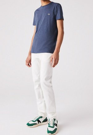 Granatowy T-shirt z okrągłym dekoltem z zielonym logo, zestawiony z białymi, dopasowanymi jeansami oraz zielonymi sneakersami z białymi i czarnymi detalami.