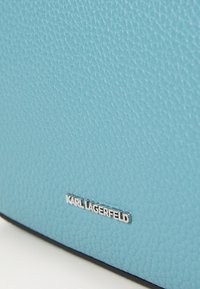 Light blue textured leather bag with a silver "KARL LAGERFELD" logo on the front, featuring a smooth black bottom edge.