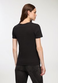 Czarny t-shirt z krótkim rękawem wykonany z bawełny, z klasycznym okrągłym dekoltem i dopasowanym krojem, noszony z ciemnoniebieskimi dżinsami.