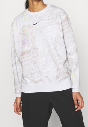 Personne portant un sweat-shirt Nike blanc avec un motif marbré multicolore subtil et un pantalon noir, debout devant un fond blanc uni.