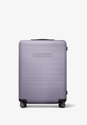 Valise rigide de couleur violet clair avec une finition mate, présentant des rainures horizontales, une poignée supérieure et quatre roulettes noires.